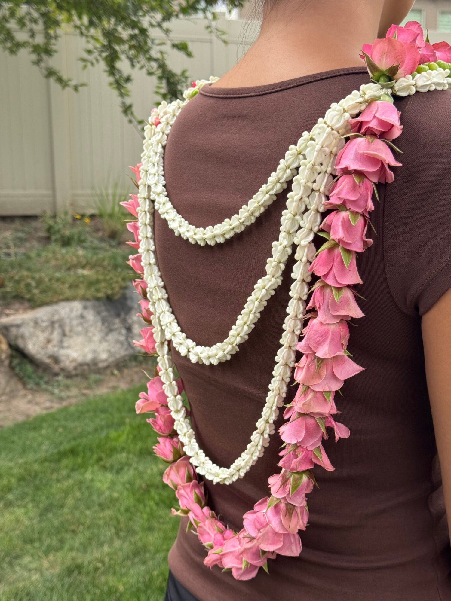 Person wearing a dark dress decorated with pink flowers and white trim, standing outdoors.