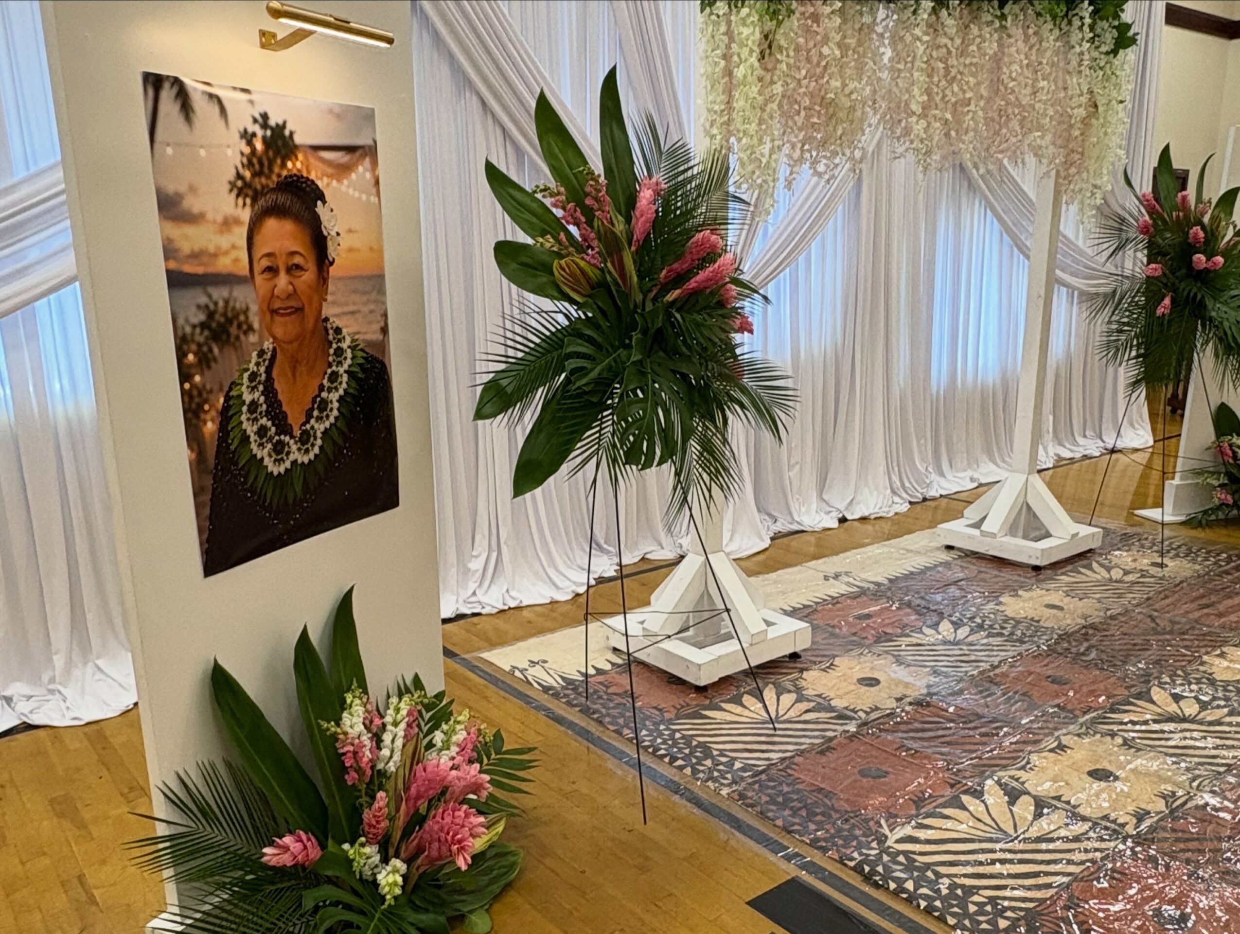 A framed portrait beside floral arrangements and white drapery at an indoor event.
