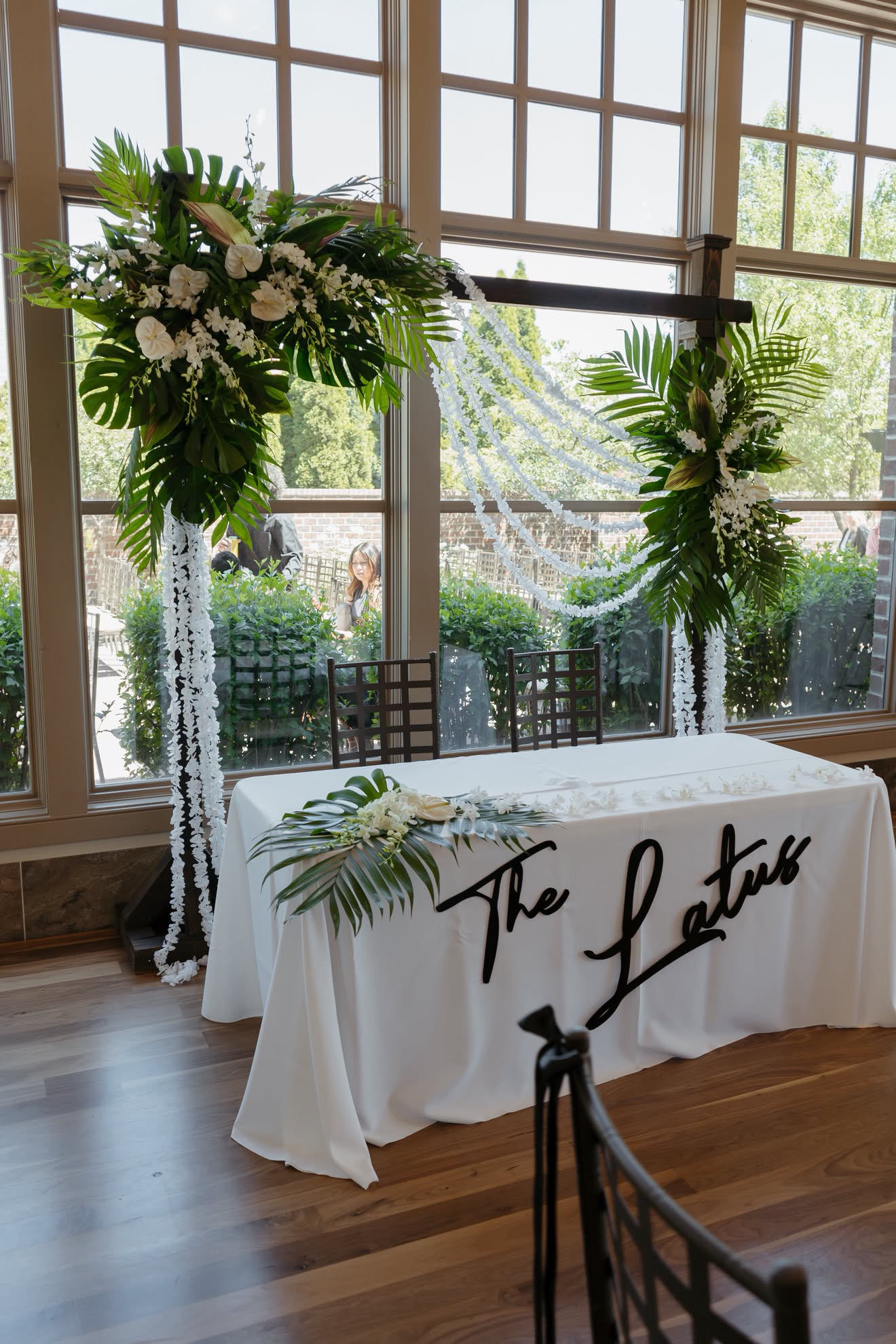 Floral arrangements frame a white tablecloth with the words “The Love” in a bright room with large windows.