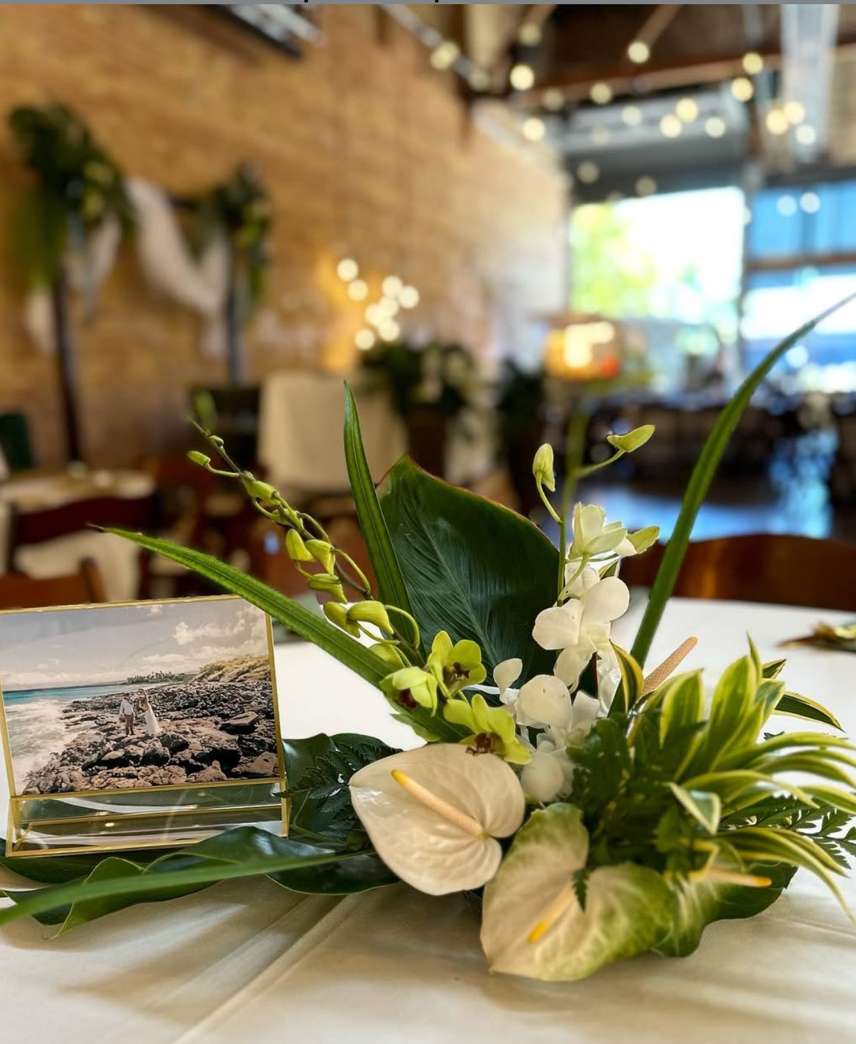 Flower arrangement with white blooms and greenery on a restaurant table, with a framed photograph behind it.