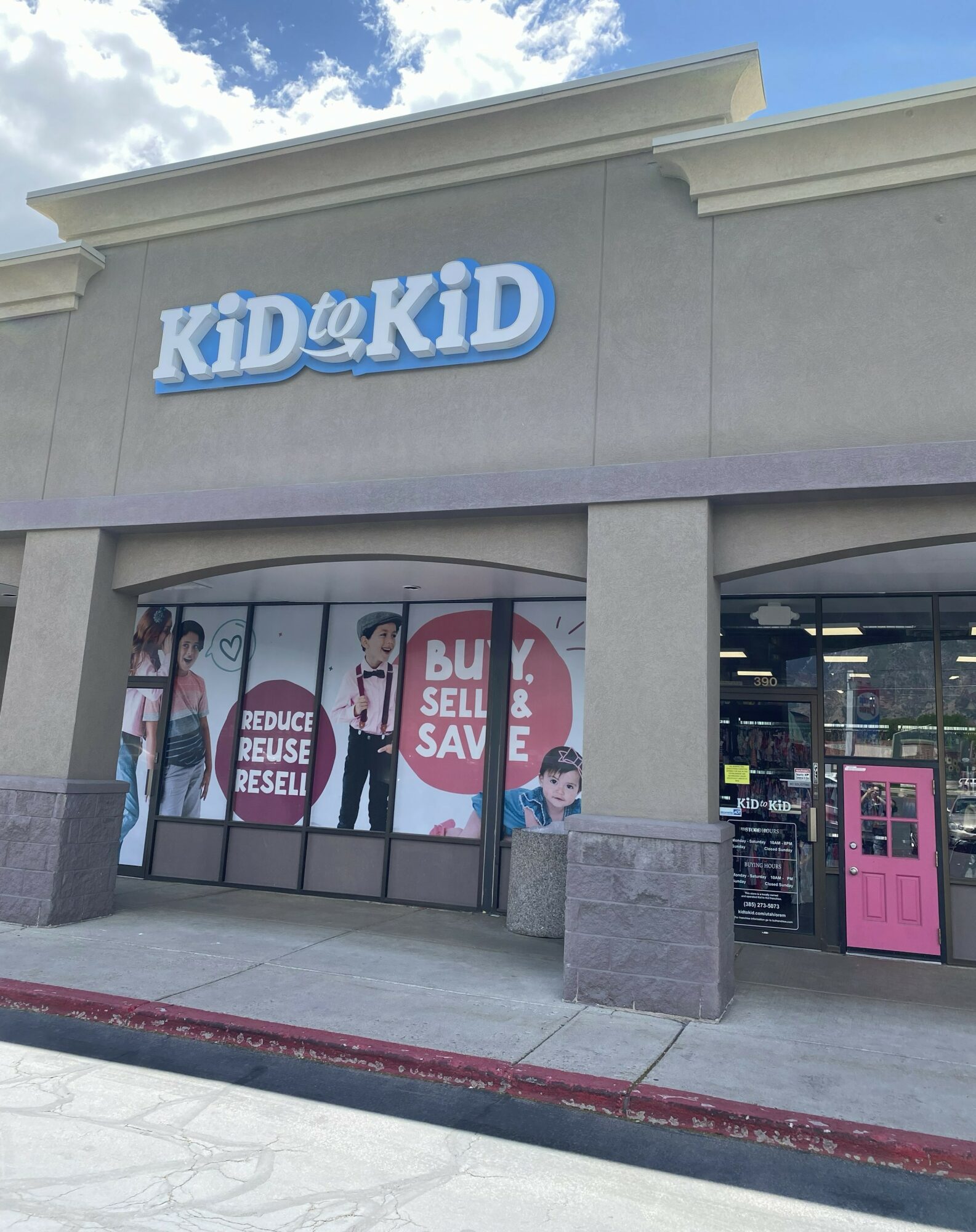 Storefront with a sign reading 'KID@KID' and window display with children and sale messages, under a blue sky.