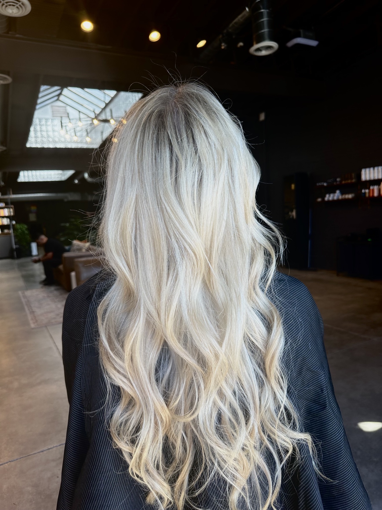 Back of a person with long, wavy, platinum blonde hair in an indoor space with high ceilings and large windows.
