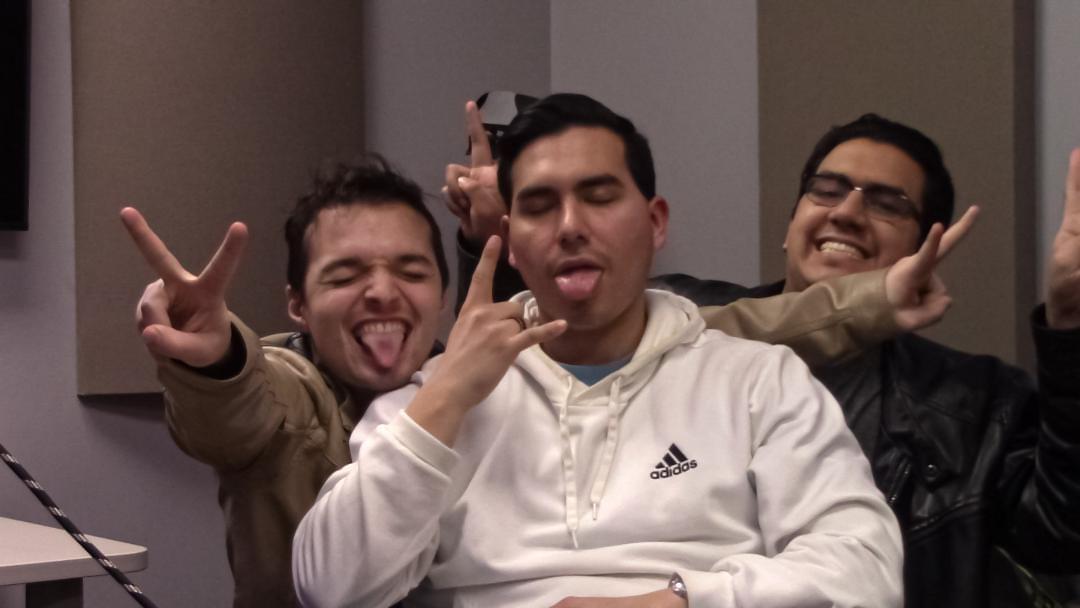 Three people making playful gestures, sticking out tongues and smiling, in an indoor setting.