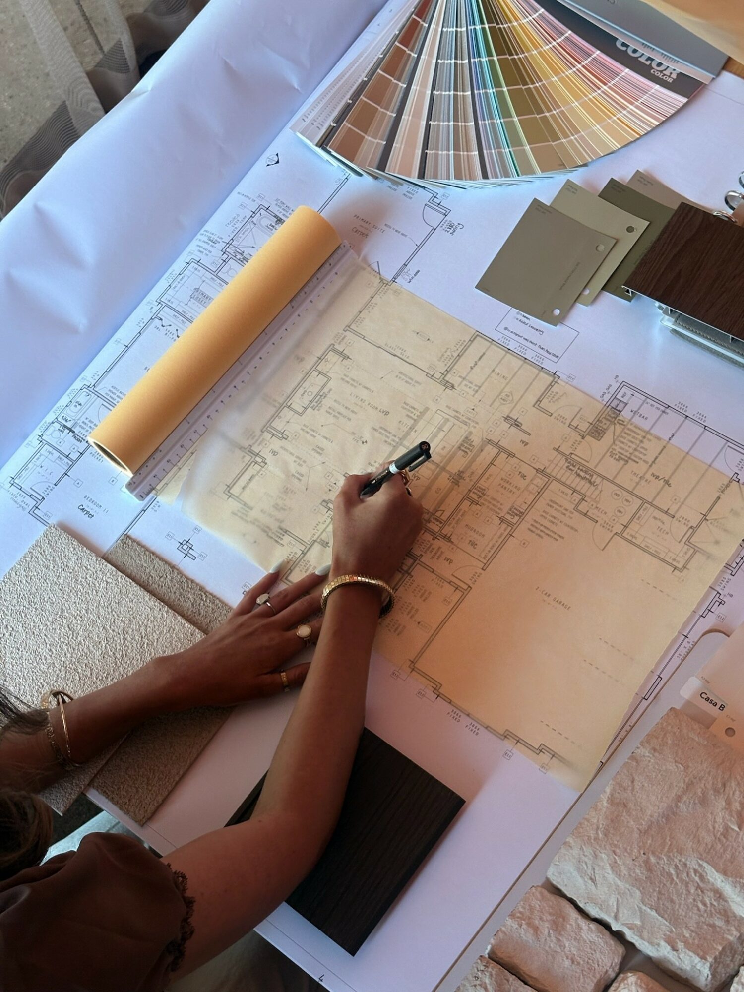 Person's hand drawing on architectural blueprint with color samples and paint swatches nearby, color palette fan above.