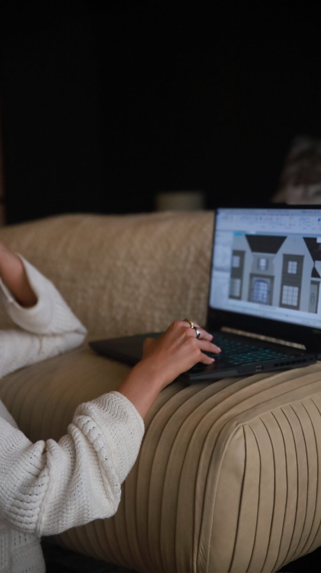 Child using a laptop on a sofa, with a building image on the screen, in a dimly lit room.