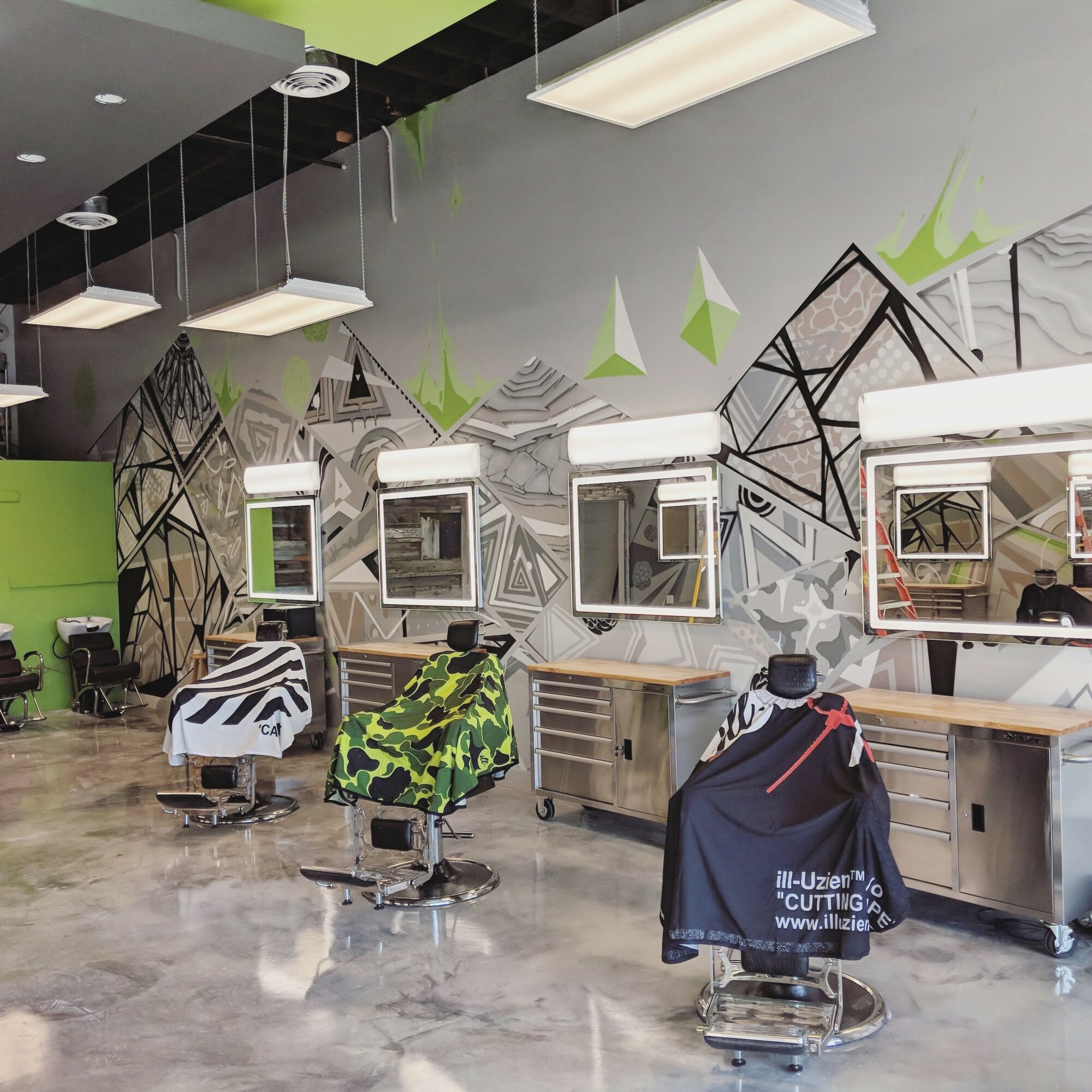 Barber chairs in a modern salon with geometric wall art and mirrors, illuminated by ceiling lights, with a polished floor.