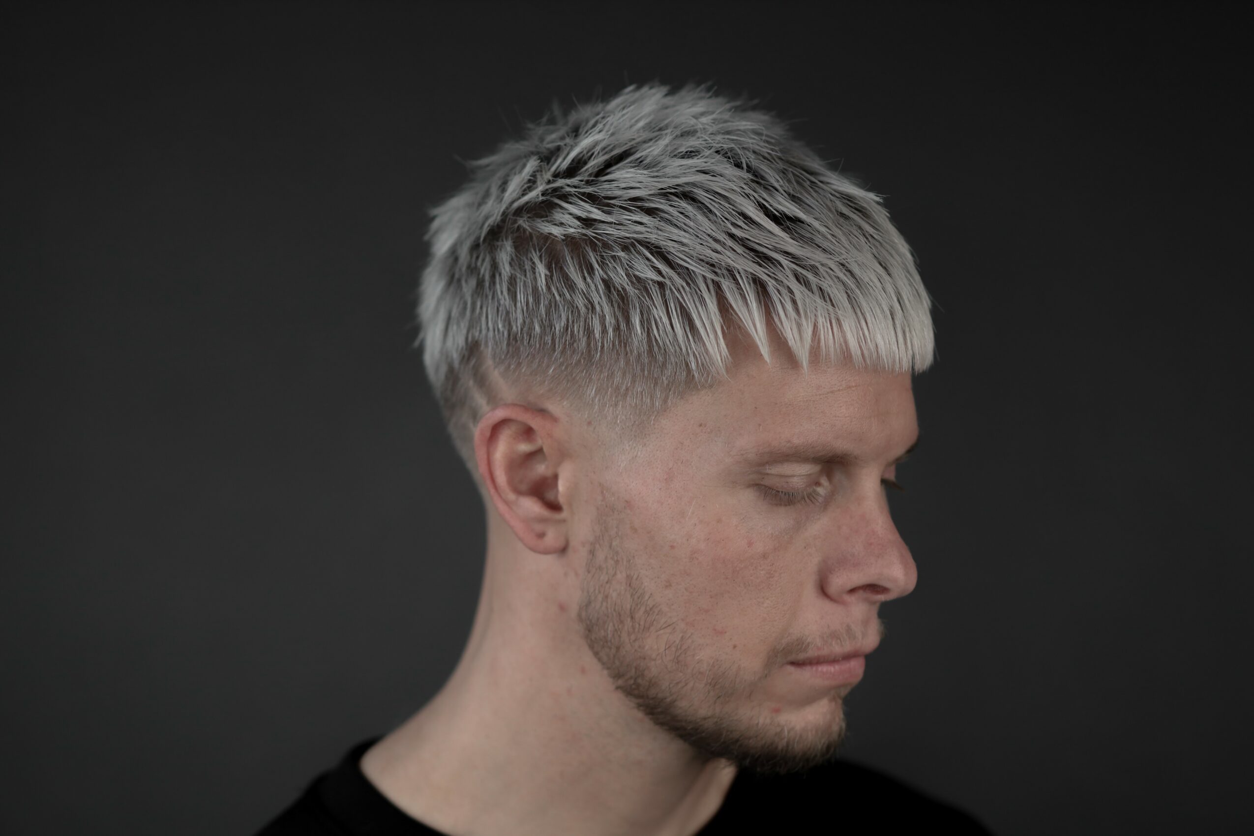 Side profile of a young man with short, light-colored hair against a dark background.