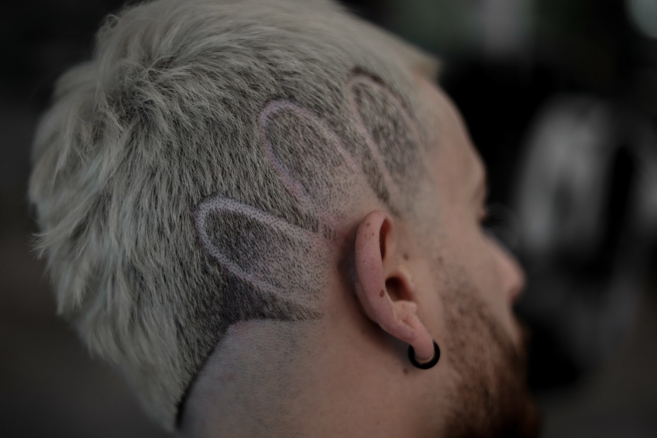 Side view of a person with short, platinum blonde hair featuring a shaved design, ear piercing, and earring.