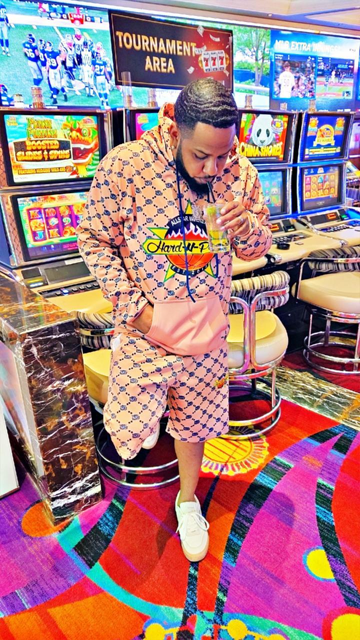 Person standing in front of slot machines in a casino, wearing a patterned outfit and white shoes, looking down.