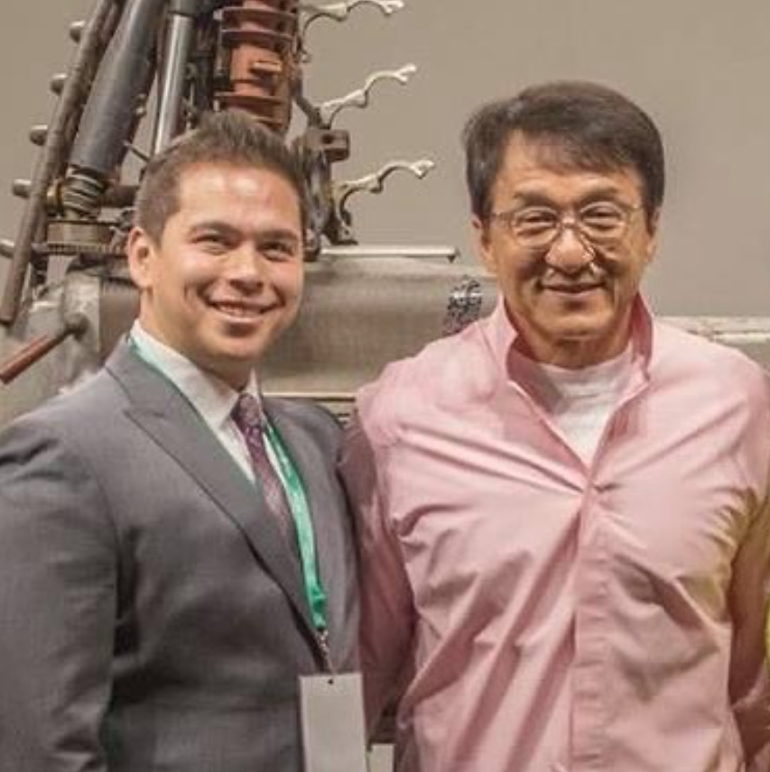 Two men standing side by side, smiling, with industrial equipment in the background.