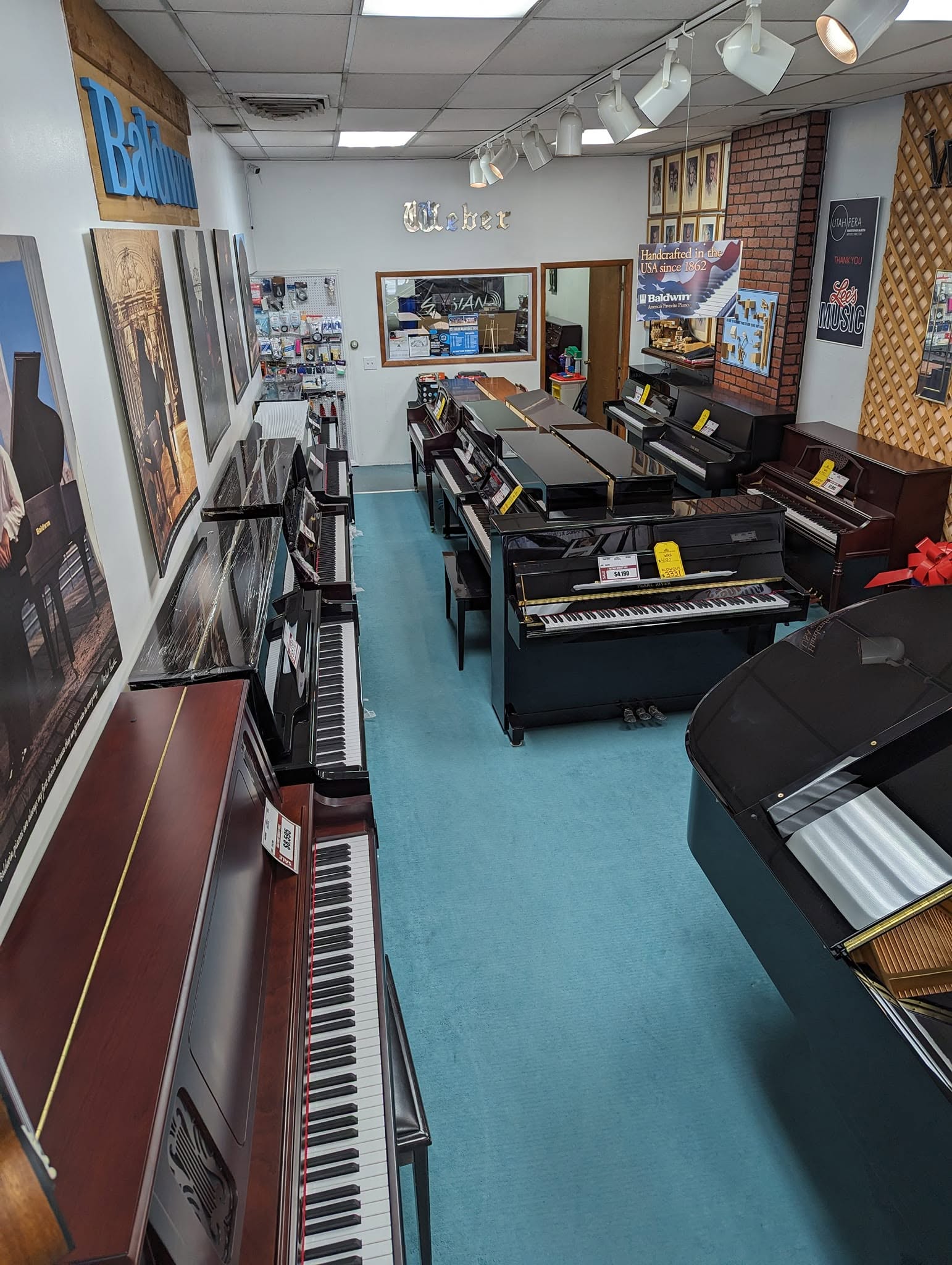 Music store with pianos and keyboards, posters on walls, and a blue floor, viewed from the entrance.