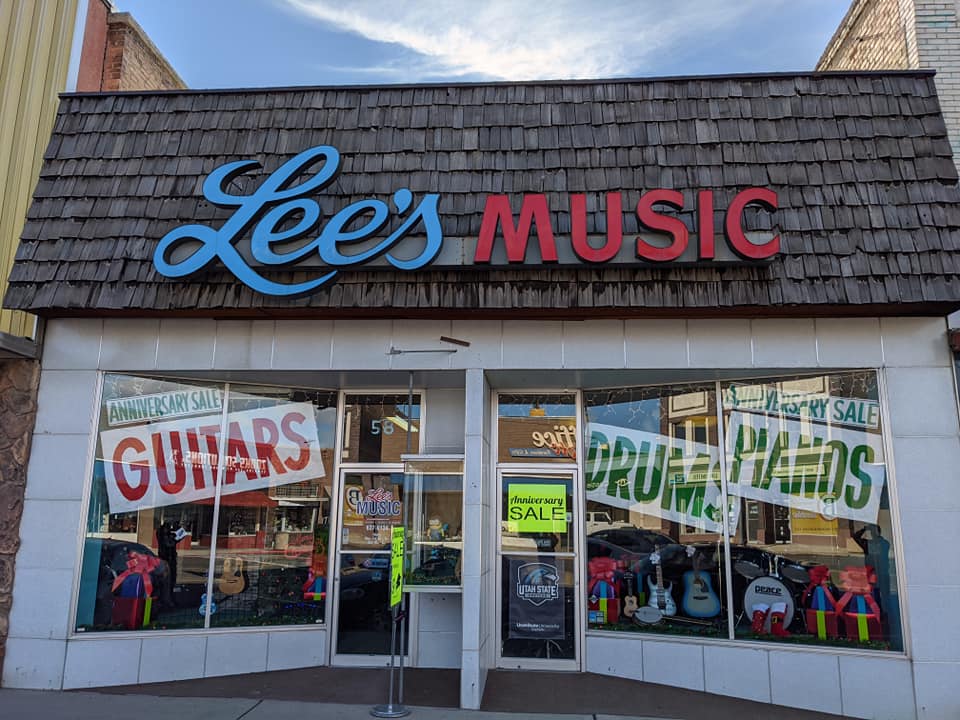 Storefront with Lee's Music sign, large windows displaying sale signs and merchandise, and a door in the center.