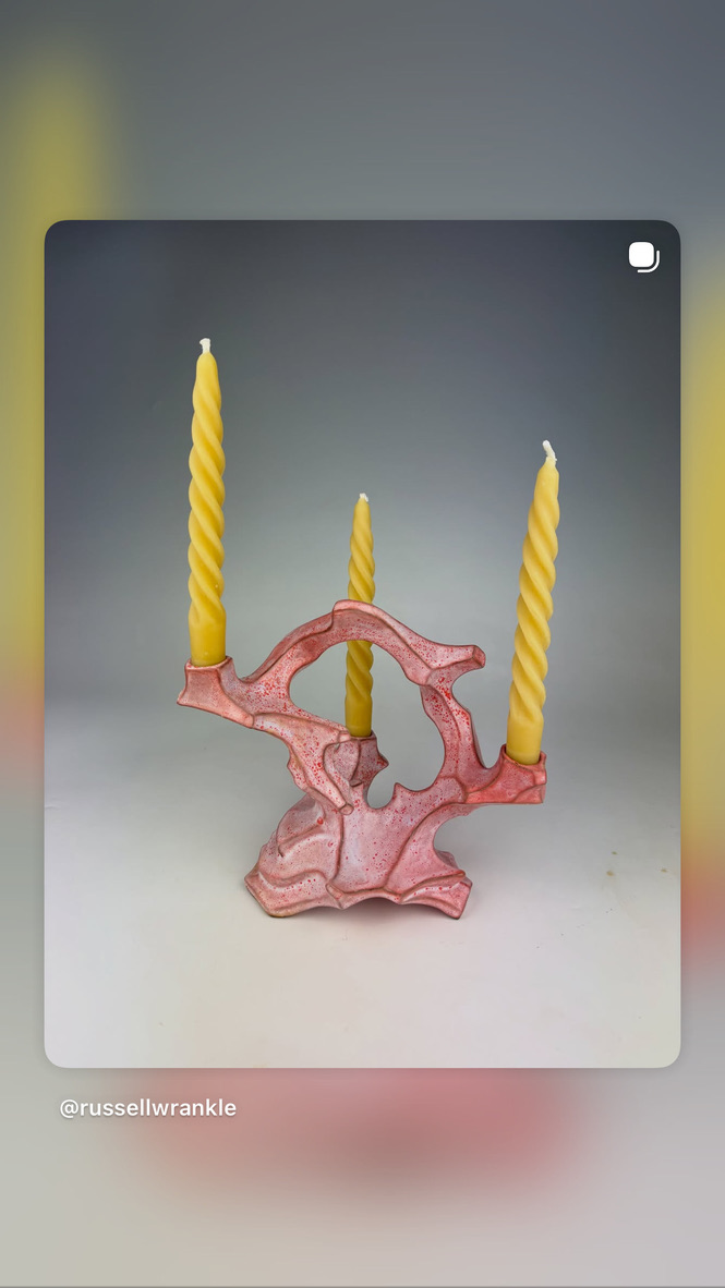 Pink sculpted candle holder with three tall yellow candles against a gray background.