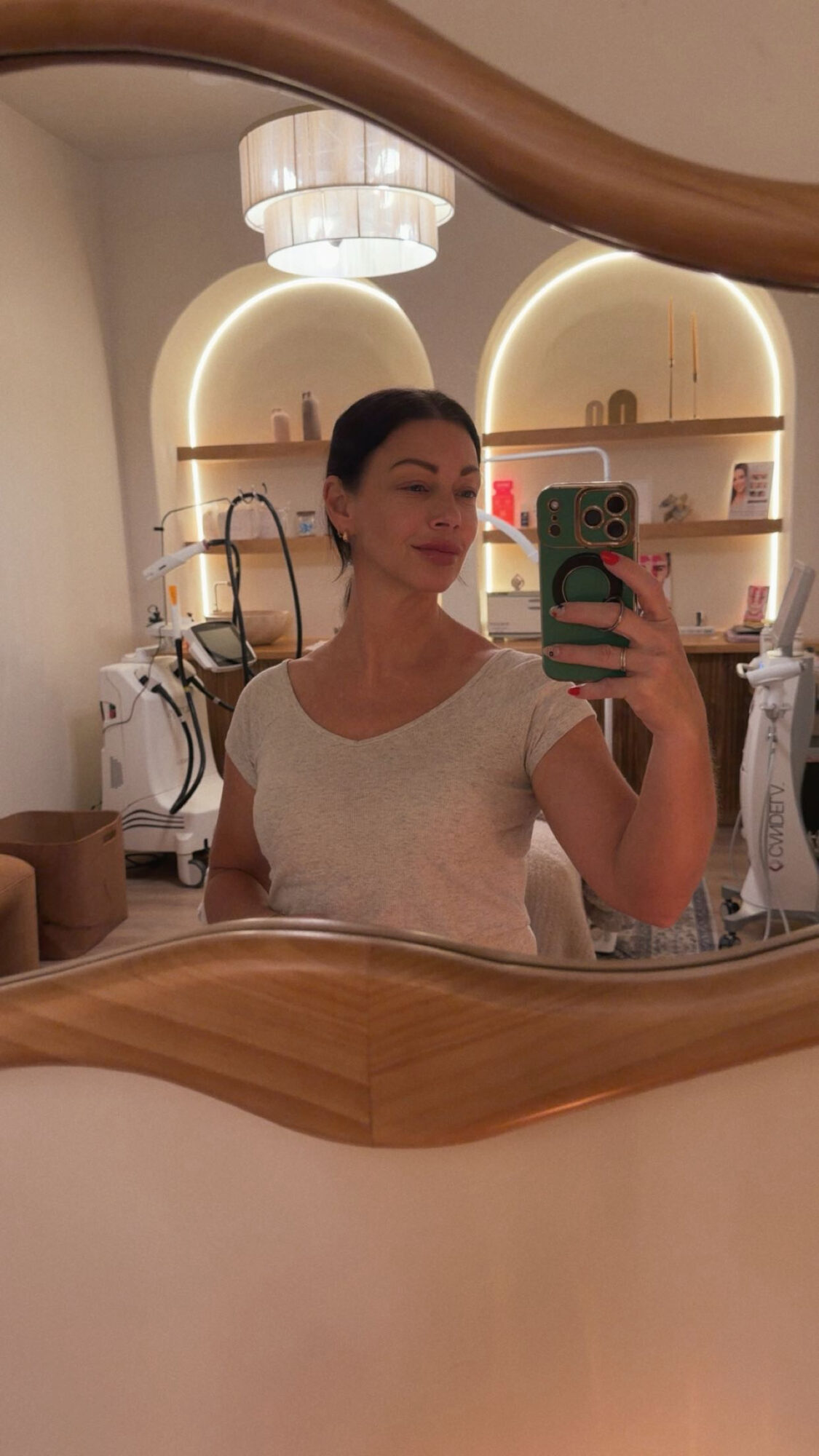 A person takes a mirror selfie in a softly lit room with shelves and salon equipment.