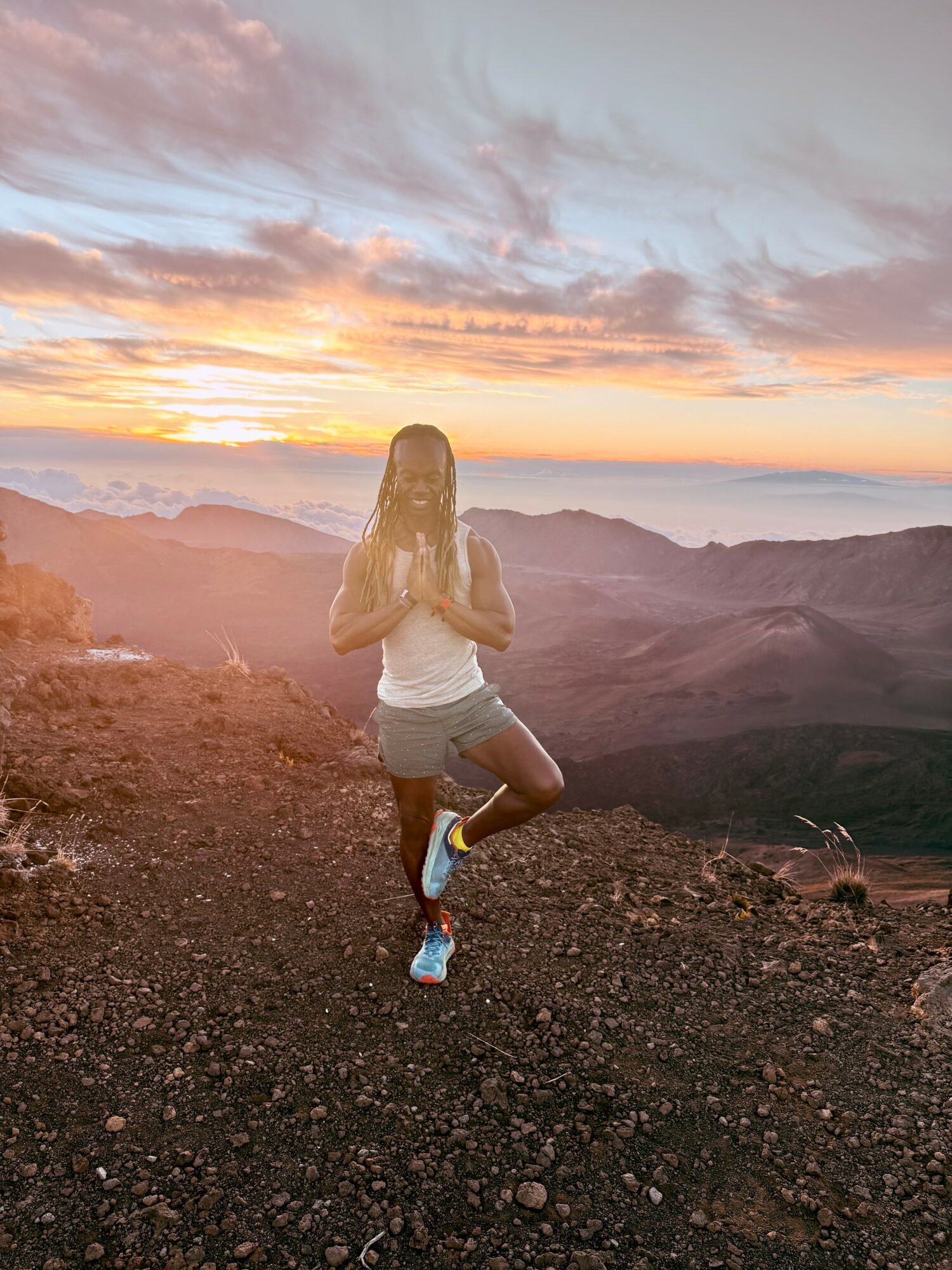 Person jogging on rocky terrain during sunset with mountains and colorful sky in background