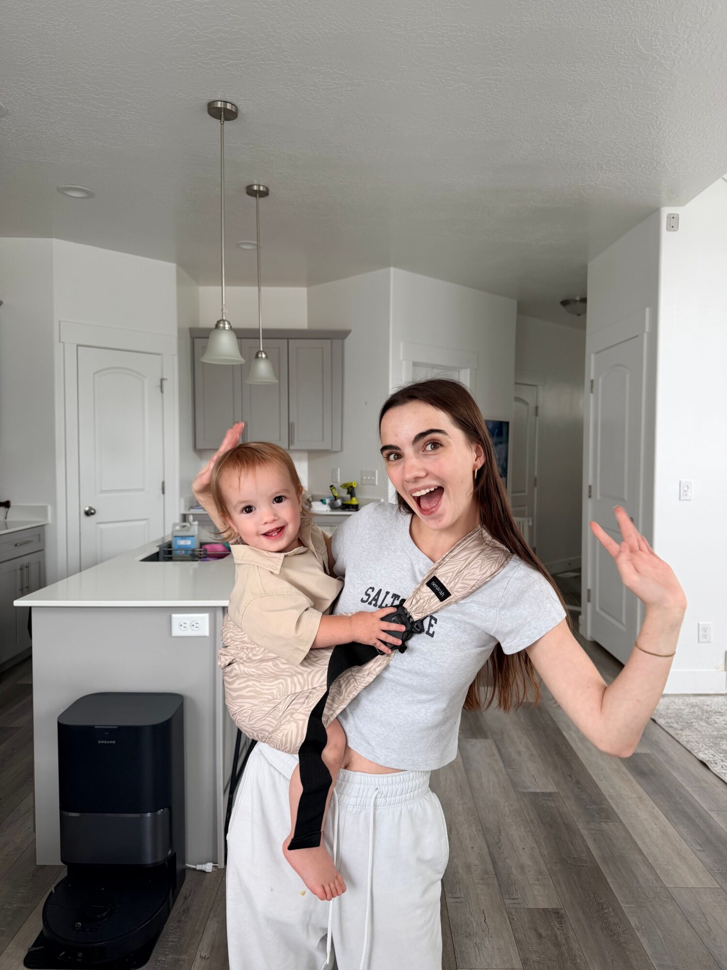Two people pose beside a kitchen island, with gray cabinets, a sink, and a black appliance nearby.