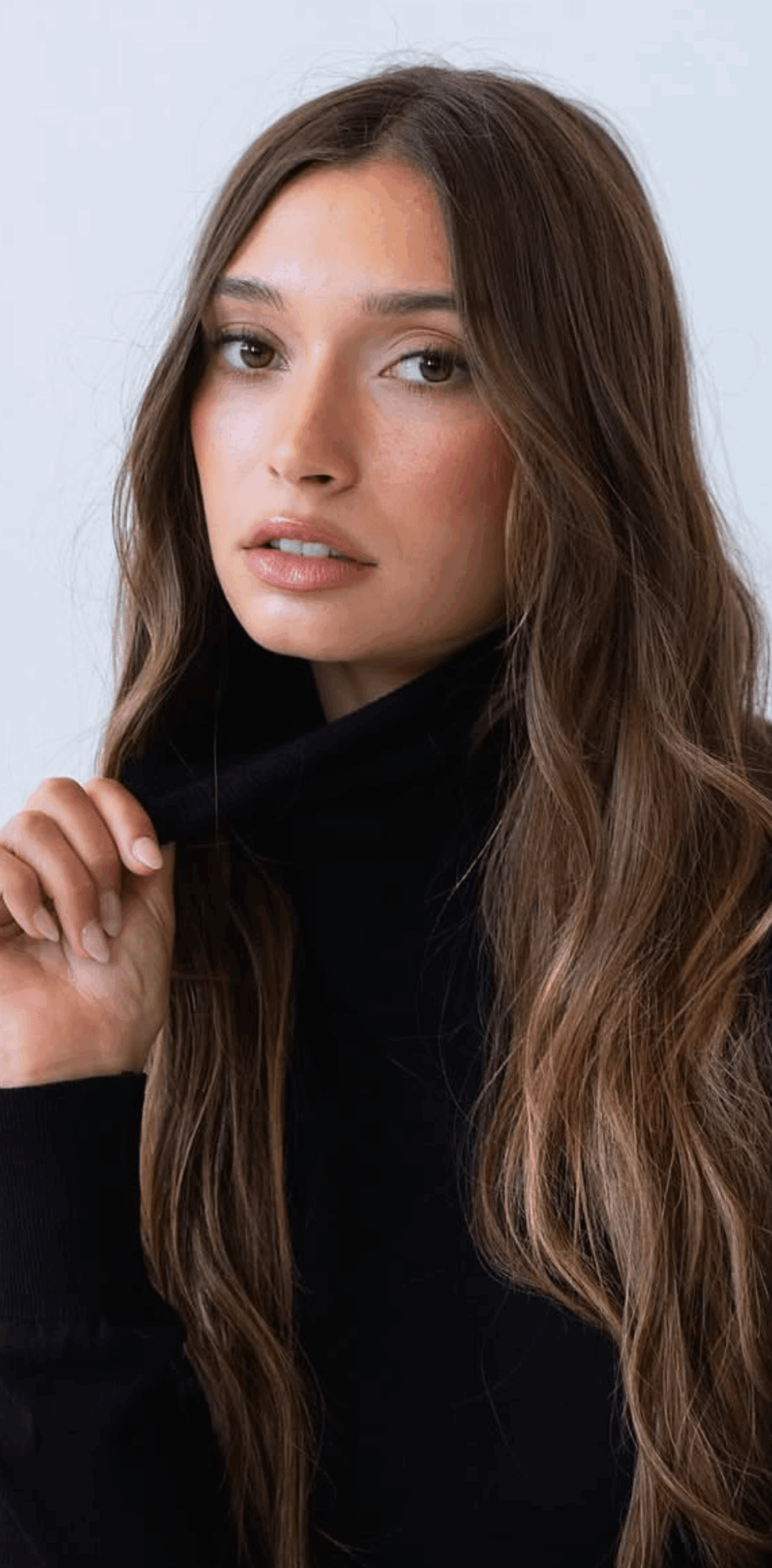 Young woman with long wavy brown hair and natural makeup, wearing a black top, looking at the camera.