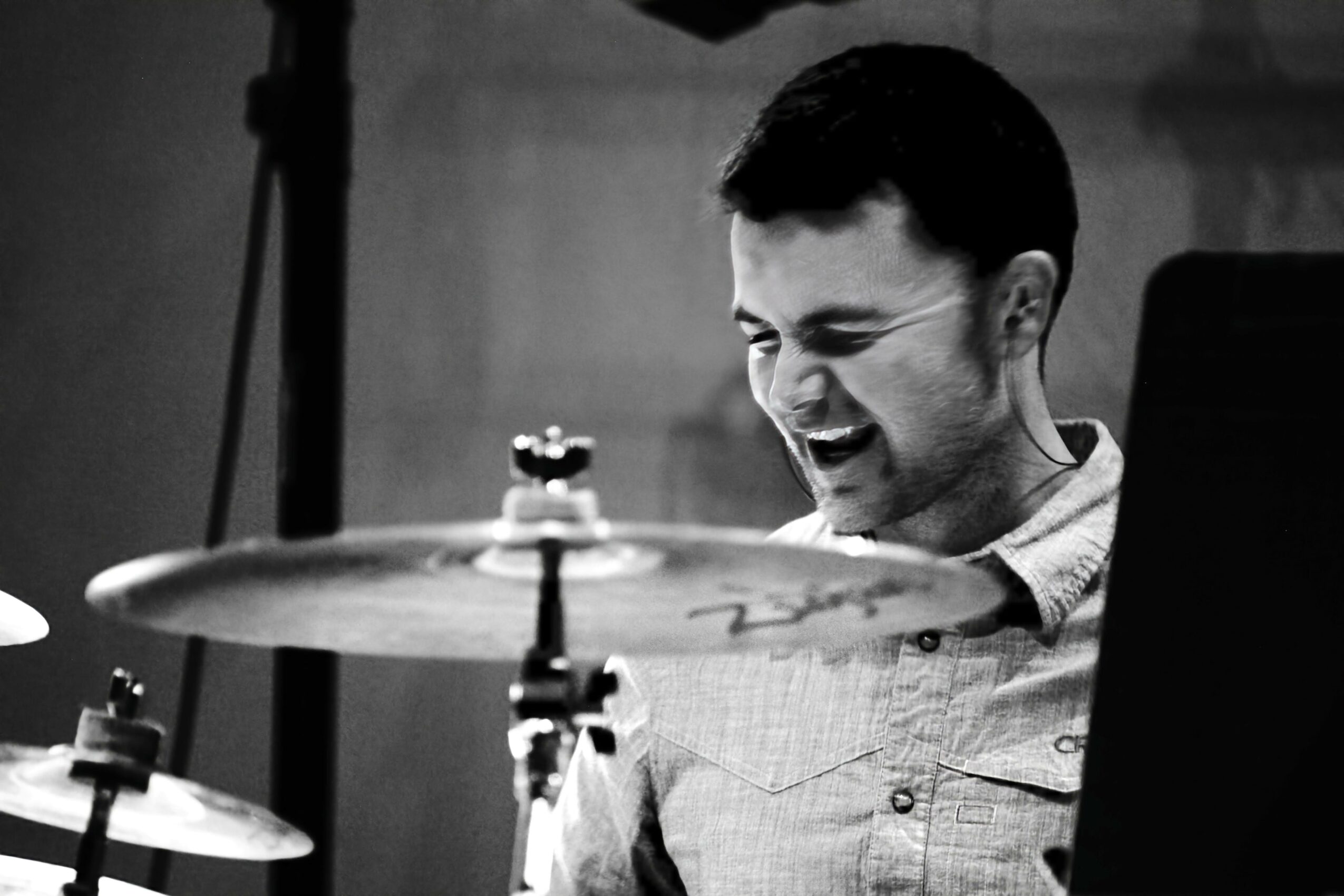 Young man smiling and playing drums in a music studio, black and white photo.