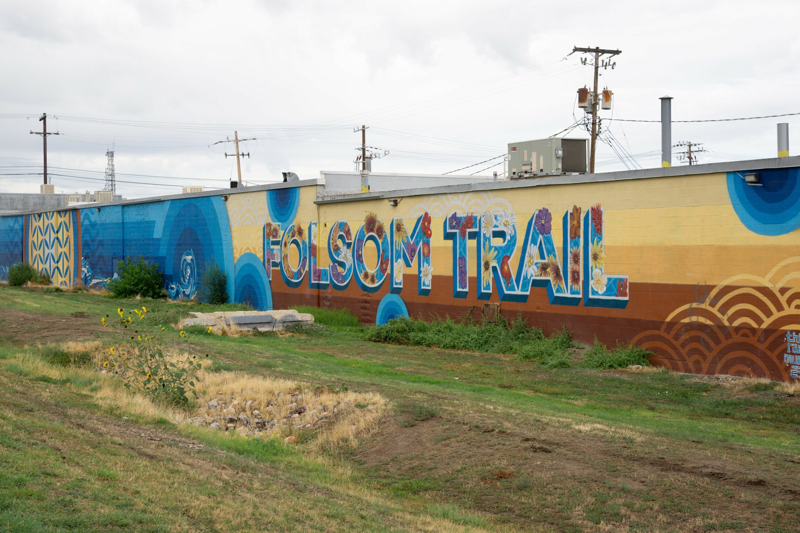 Colorful mural with the words 'OLSON TRAIL' on a wall, with power lines and sky in the background.