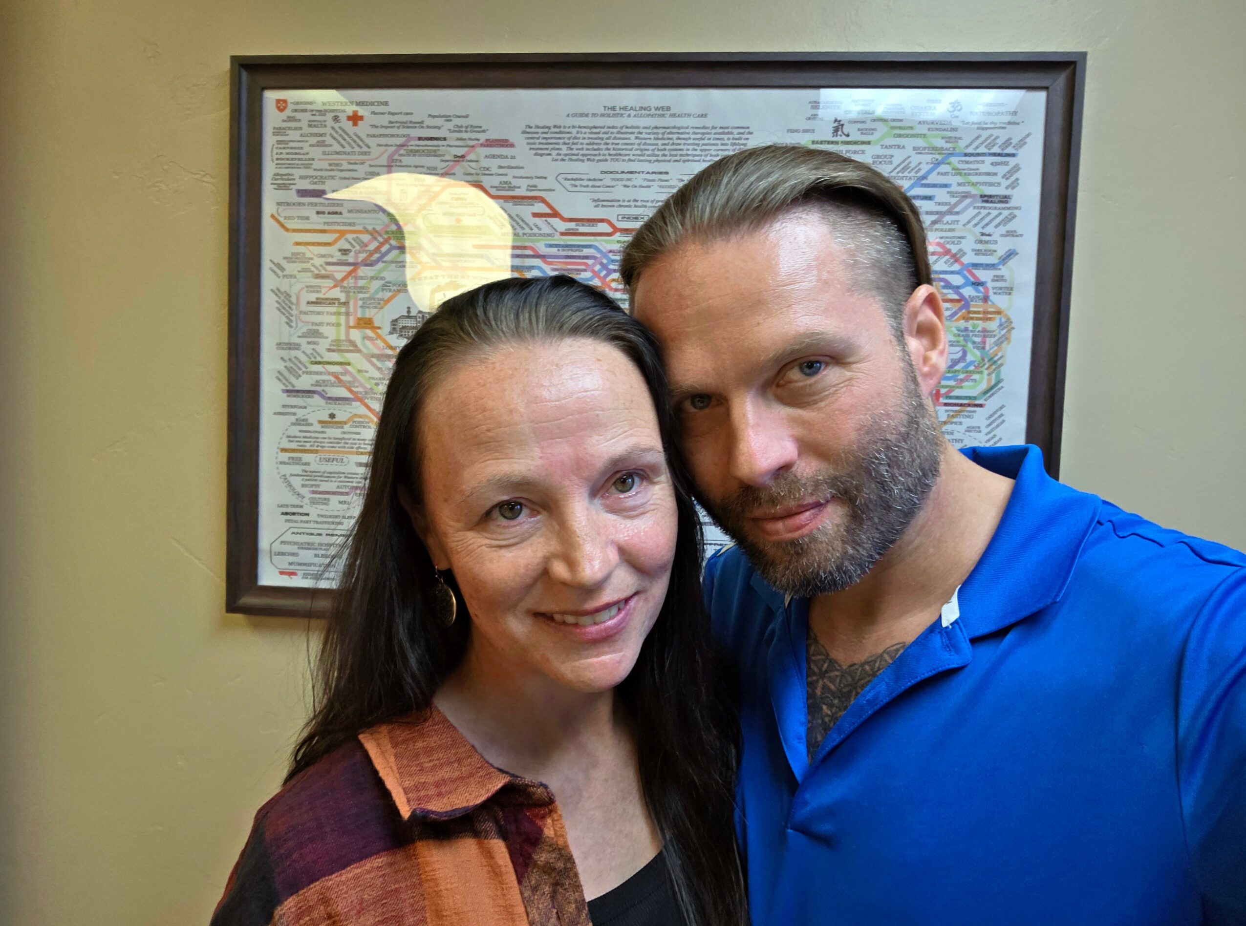 Two people, a woman and a man, pose for a photo indoors in front of a framed map on the wall.