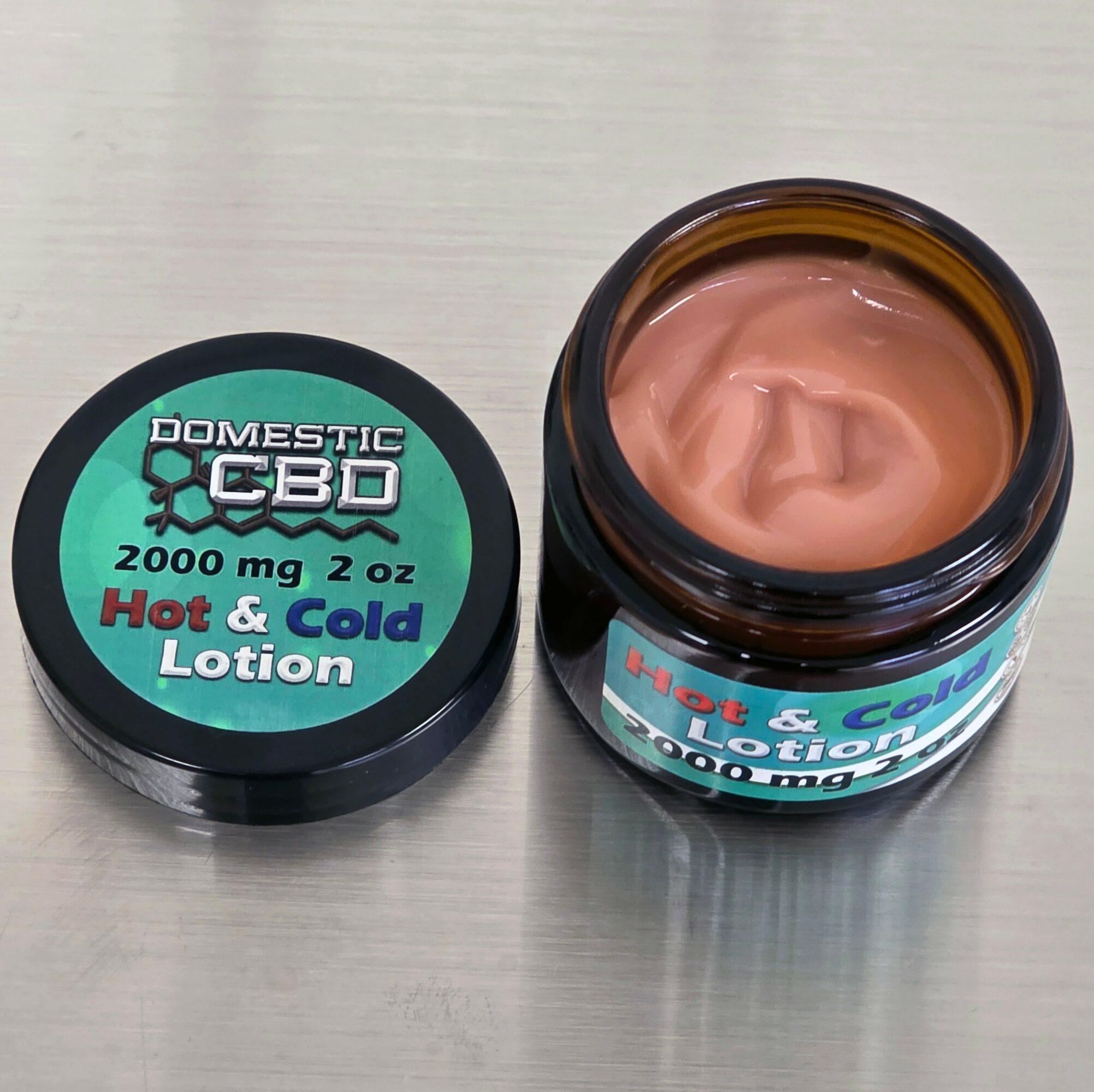 Open jar of CBD lotion with pinkish cream inside, label shows 2000 mg, hot and cold lotion, on light surface.
