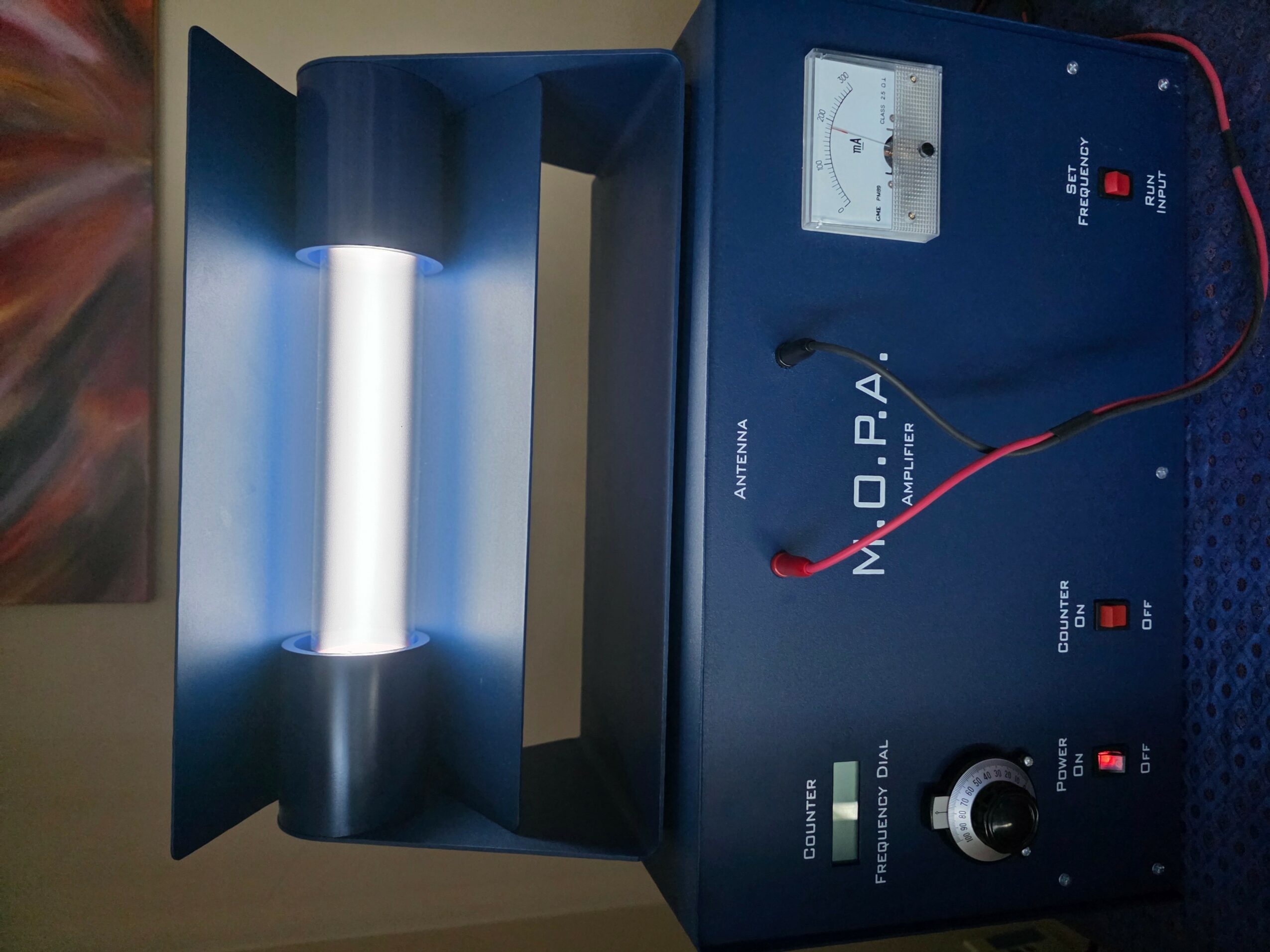 Laboratory device with a vertical cylindrical light source and control panel, blue exterior, and red and black wires connected.