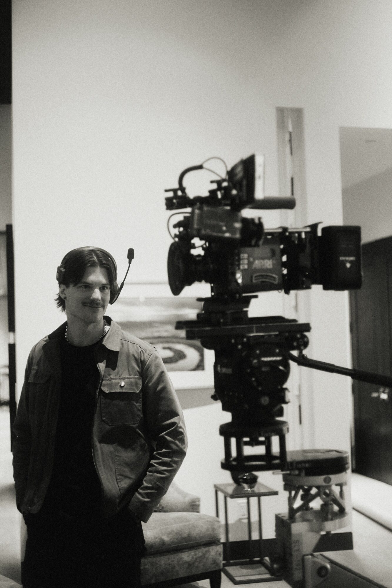 Person standing next to a large professional camera on a tripod in a room with white walls.
