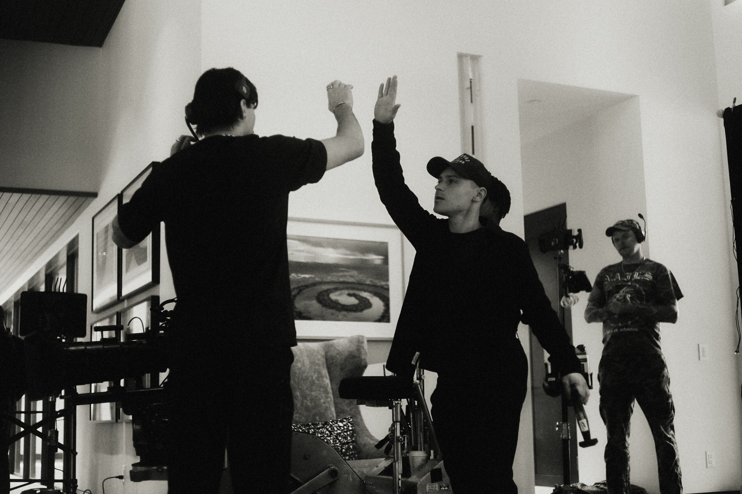 Two people high-five indoors, with a third person in the background, in a room with artwork and furniture.