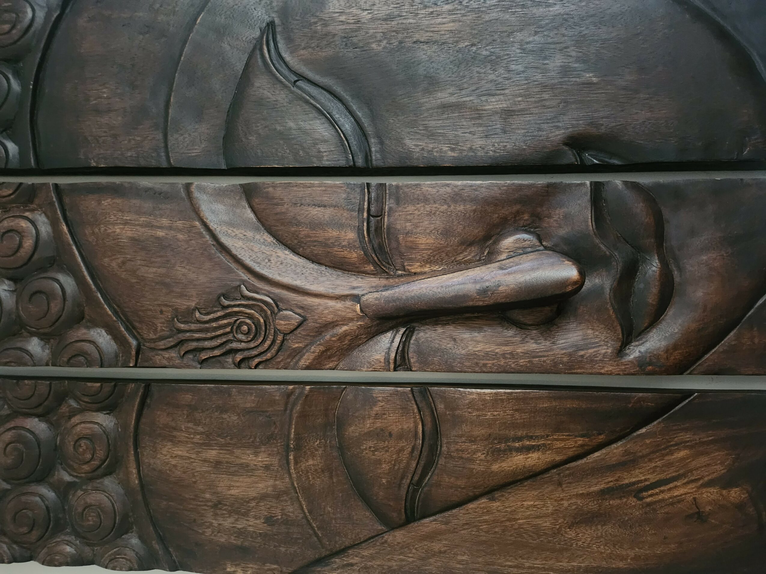 Wooden carved sculpture of a reclining figure with detailed hair and facial features, horizontal orientation.
