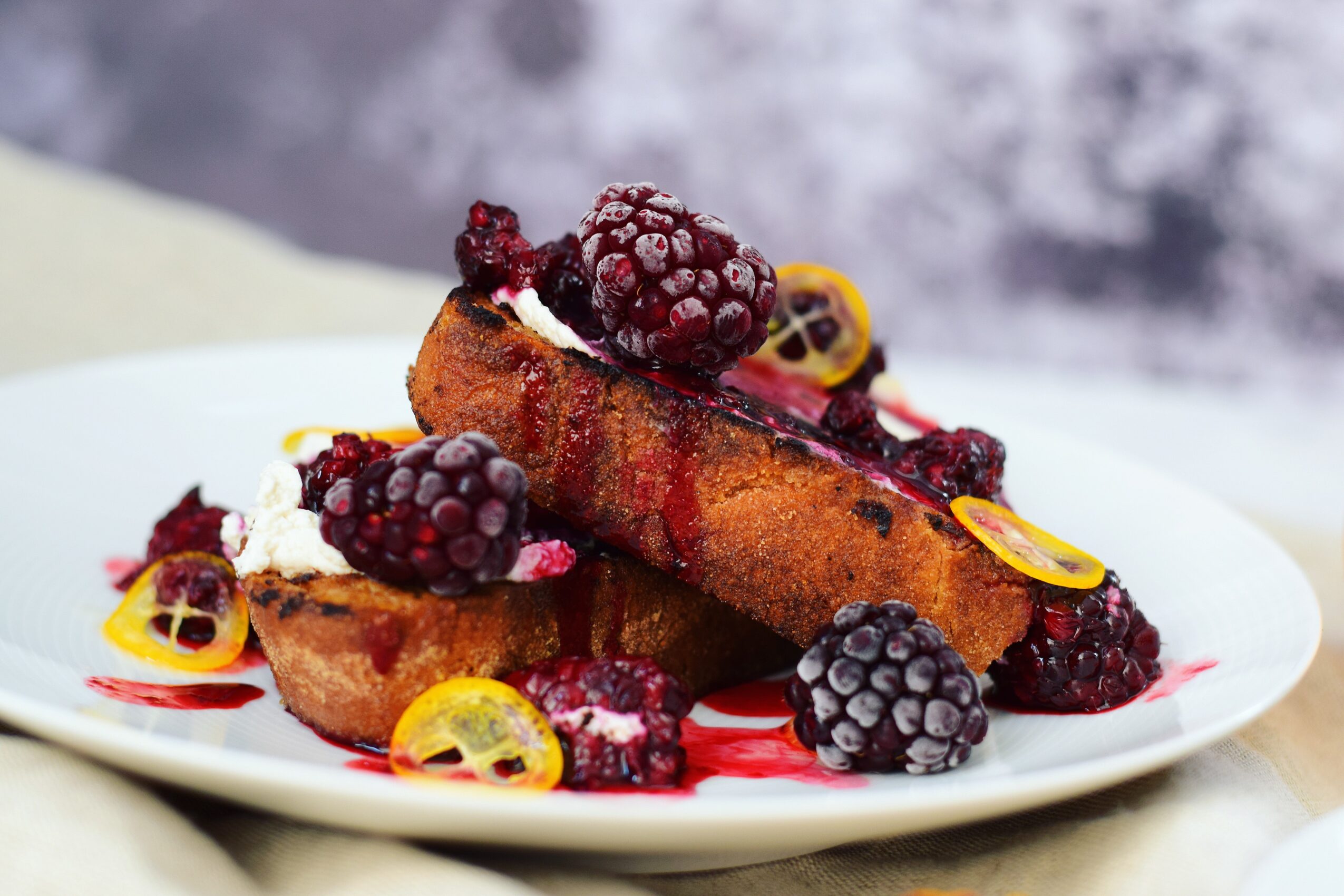A plated dessert topped with berries, citrus slices, and red sauce.