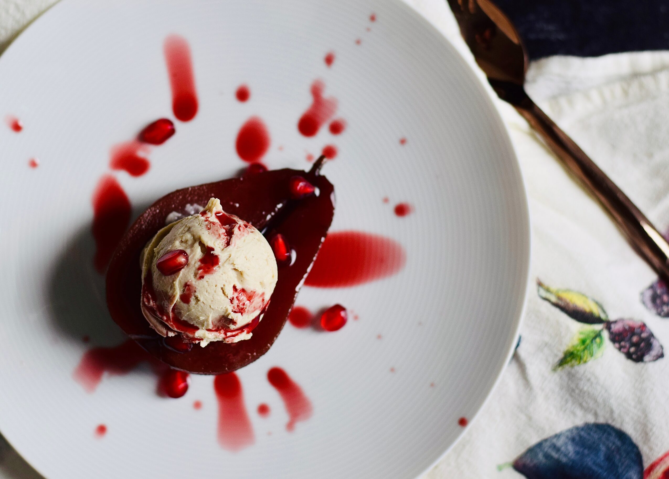 A scoop of ice cream in a dark bowl sits on a white plate splattered with red sauce.