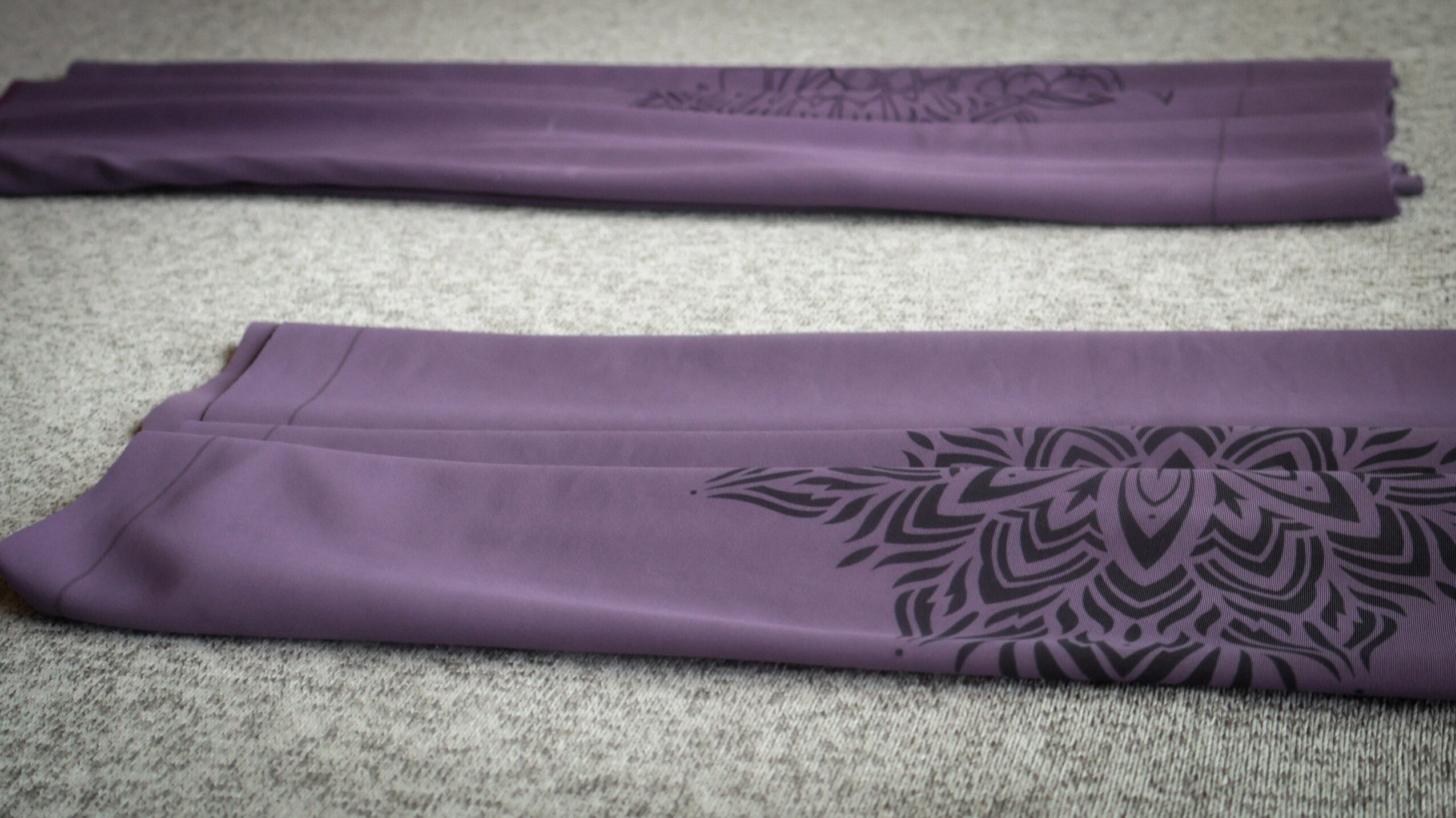 Two folded purple fabric pieces with dark decorative patterns on a light textured surface.