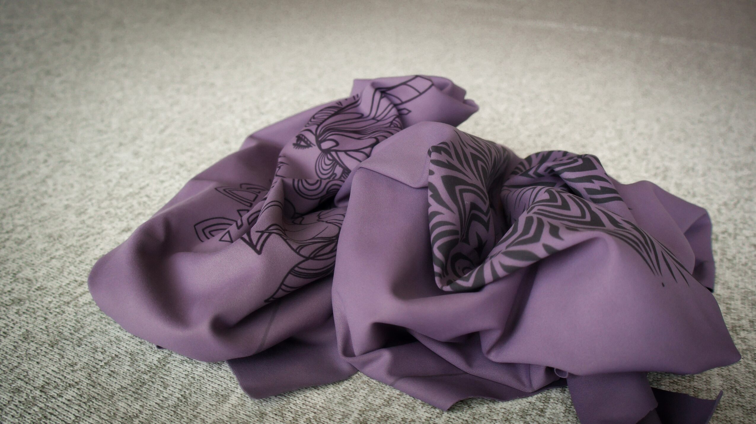 A crumpled purple fabric printed with dark abstract patterns lies on a light textured floor.
