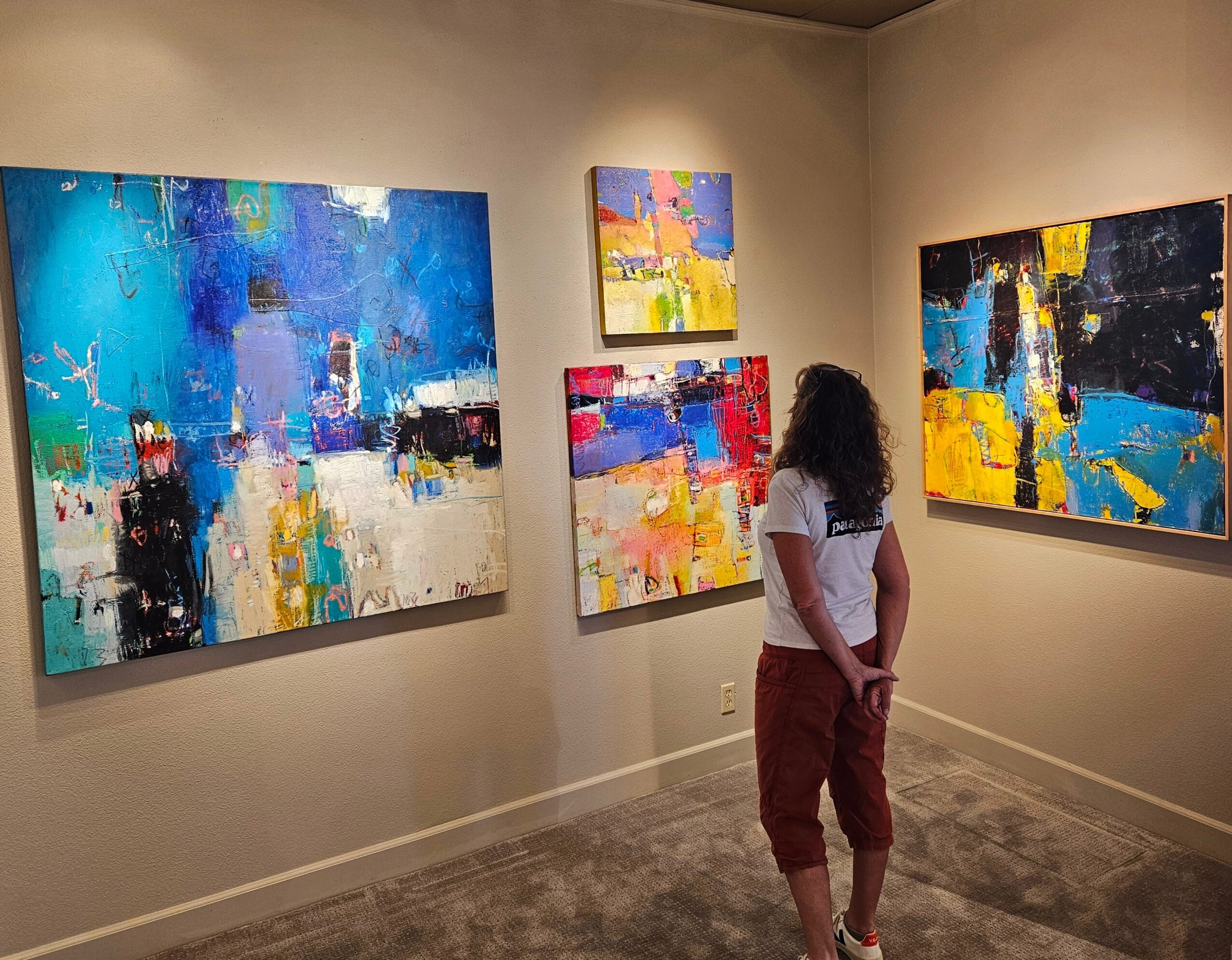 Person viewing colorful abstract paintings displayed on gallery walls.