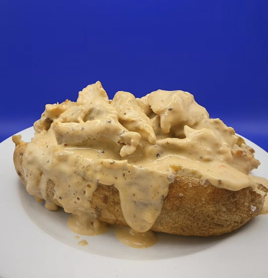 A baked potato on a white plate is topped with a thick, creamy sauce against a blue background.