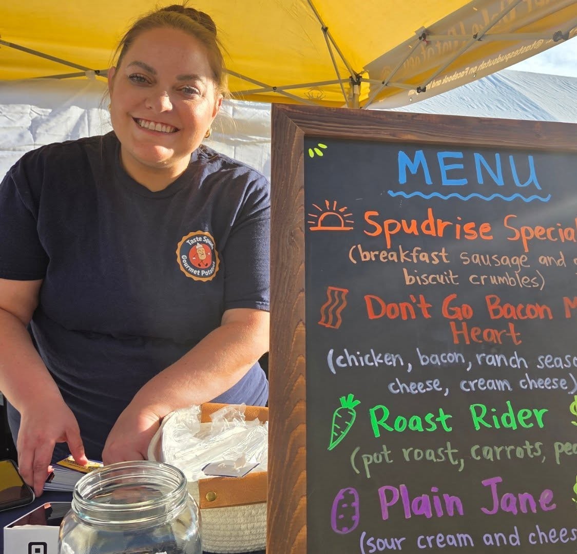 A smiling person stands beside a colorful menu board under a yellow canopy.