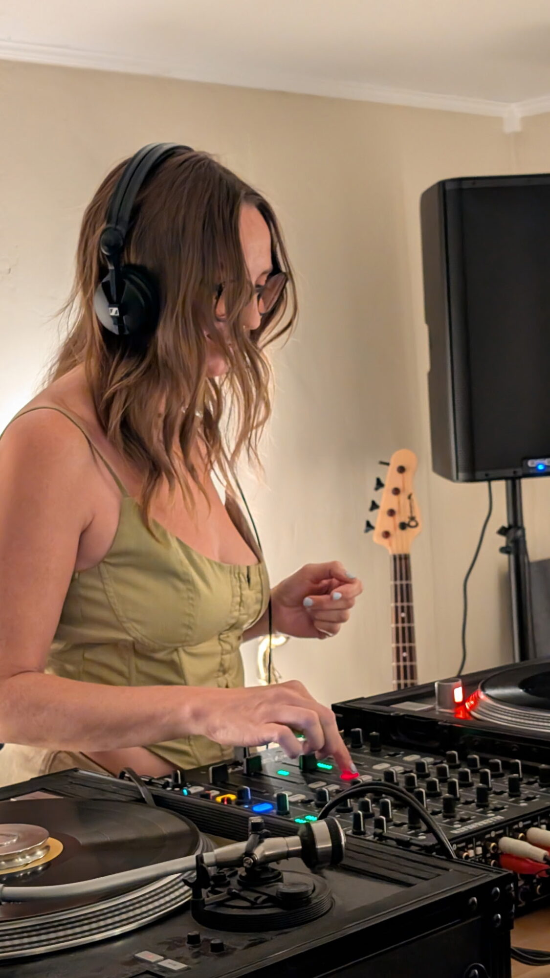 A person wearing headphones operates a DJ mixer beside a turntable and speaker.