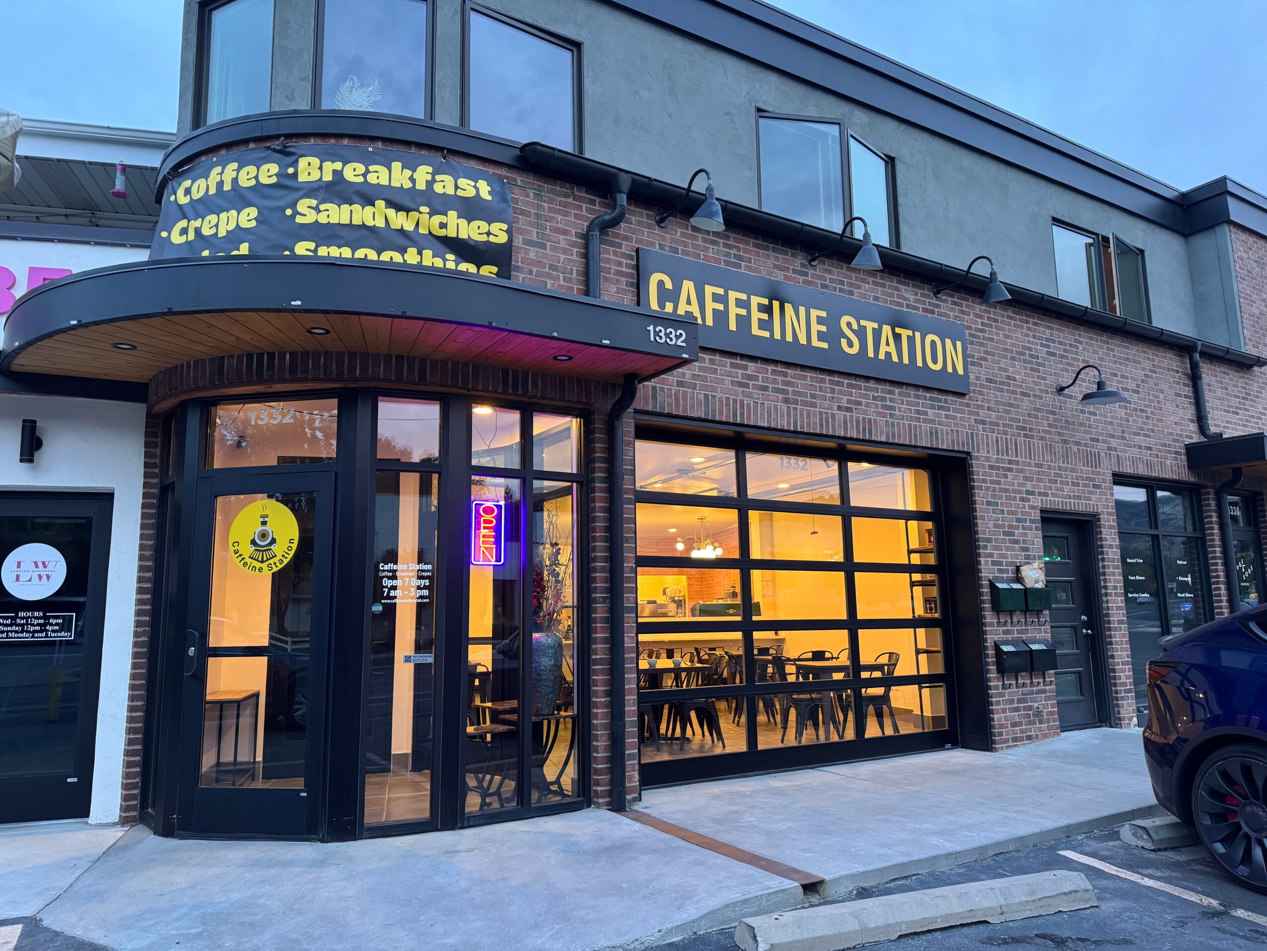Street-level view of a café storefront with large windows, outdoor signage, and a parked car.