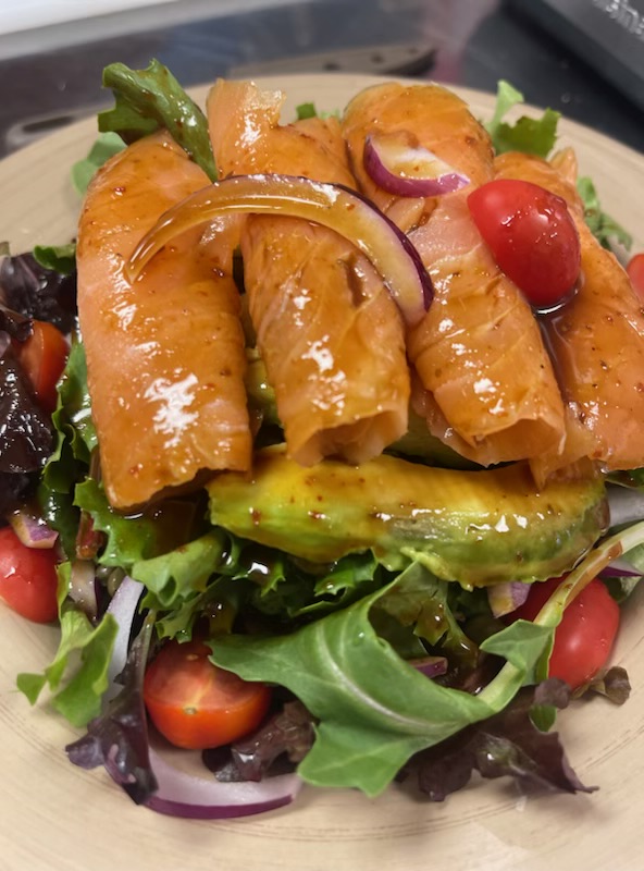 Plate of glazed salmon with leafy greens, tomato, onion, and sliced vegetables.
