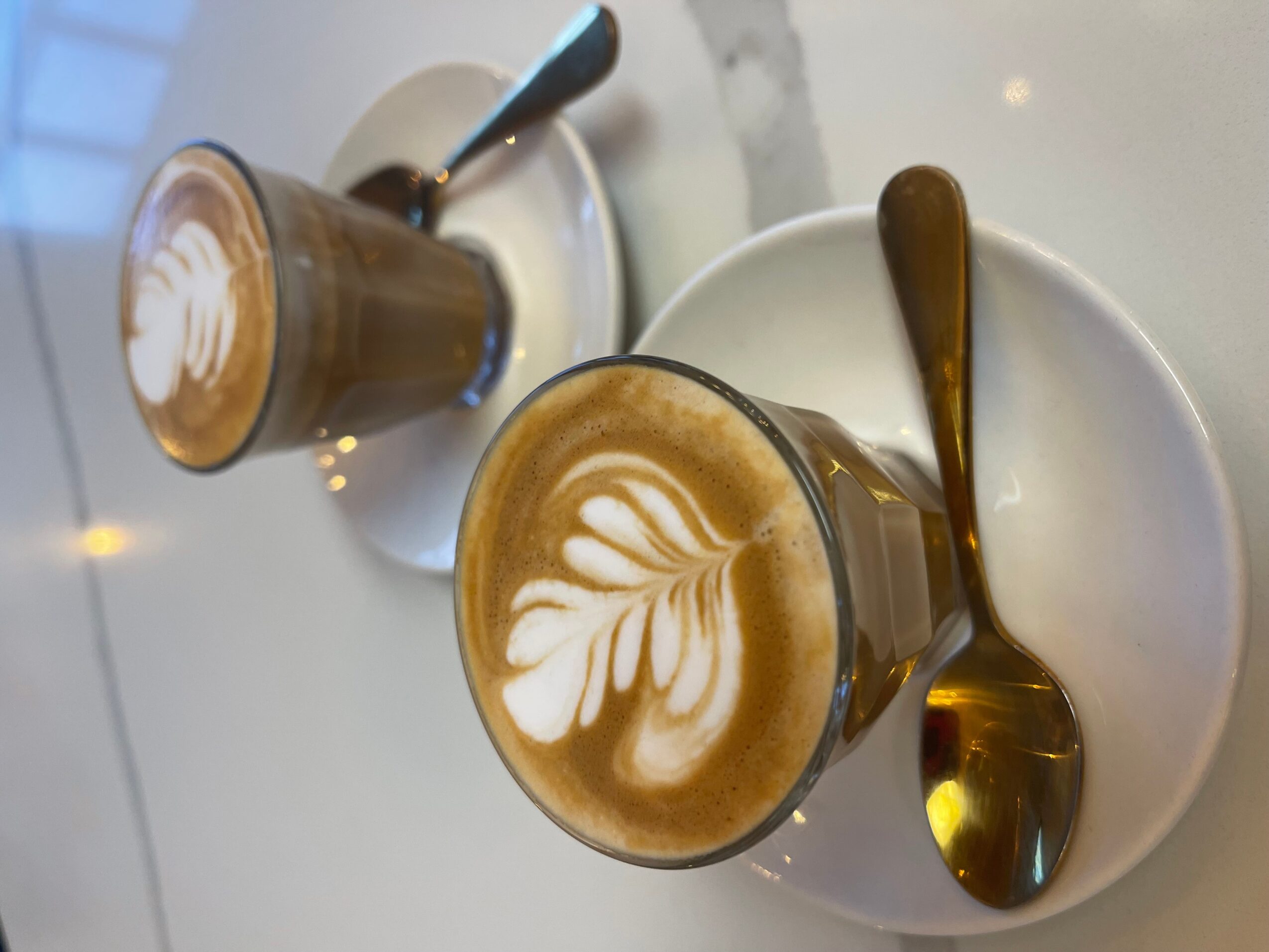 Two cups of coffee with latte art sit on white saucers beside spoons.