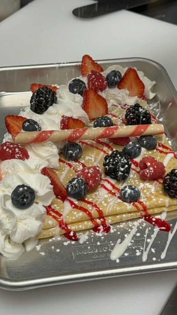 A rectangular tray of rolled ice cream topped with berries, whipped cream, and red syrup.
